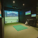Indoor golf simulator room featuring the Foresight Falcon overhead launch monitor above a hitting mat, with immersive virtual gameplay on screen.