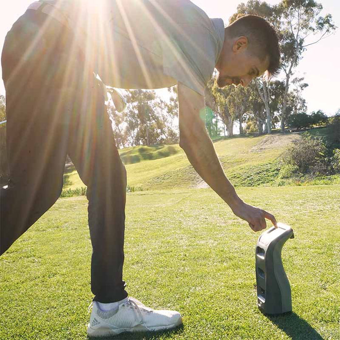 Golfer powering on the Foresight GC3 Launch Monitor under bright sunlight during outdoor practice.