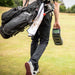 Golfer walking across the fairway carrying the Foresight GC3 Launch Monitor by hand alongside a golf bag.