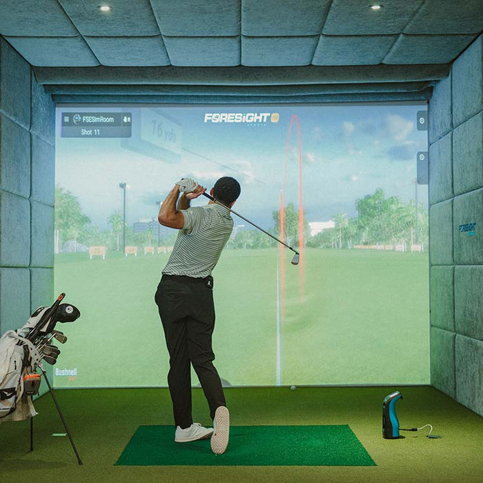 Golfer finishing swing in indoor golf simulator using Foresight GC3S Launch Monitor, tracking ball flight and performance metrics.