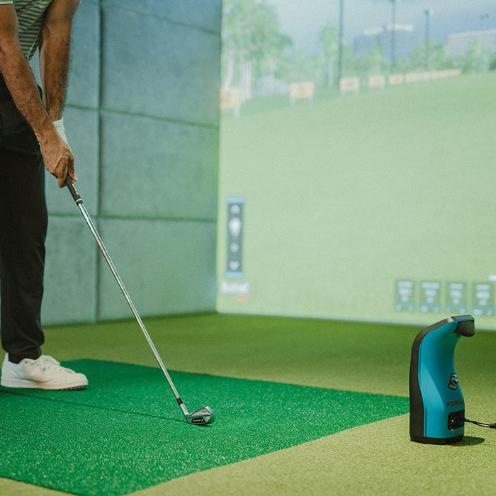Golfer preparing to hit iron shot in indoor simulator with Foresight GC3S Launch Monitor set up beside the hitting mat.