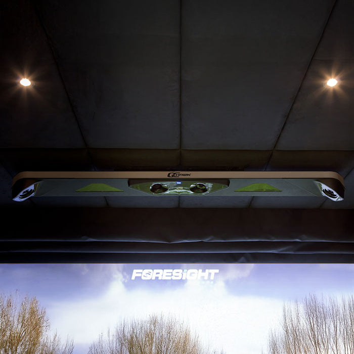 Front-facing view of the Foresight GCHawk overhead launch monitor mounted on a padded ceiling, with dual tracking lenses and ambient spotlighting.