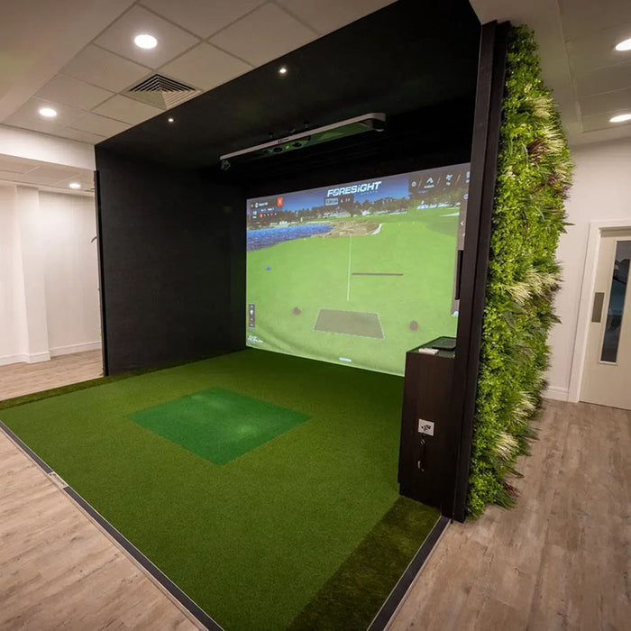 Indoor golf simulator studio with Foresight GCHawk overhead launch monitor, wall-mounted screen, and lush green hitting turf.