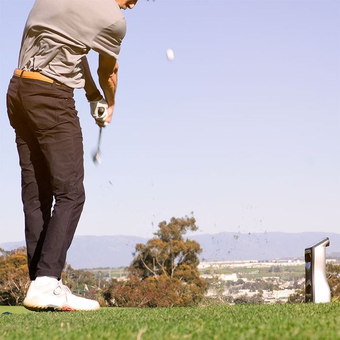 Action shot of a golfer hitting a golf ball with the Foresight GCQuad launch monitor positioned behind to capture full shot data.