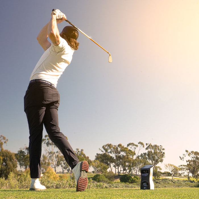 Golfer mid-swing outdoors with the Foresight GCQuad golf launch monitor positioned nearby to track real-time ball flight metrics.