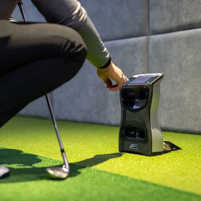Golfer crouching to adjust Foresight GCQuad Launch Monitor before hitting a shot indoors.