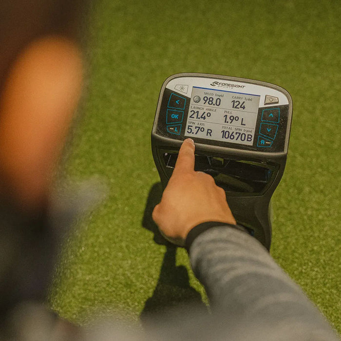 Golfer interacting with Foresight GCQuad touchscreen displaying detailed ball flight and spin metrics.