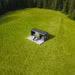 Wide aerial view of Geneva St. Moritz outdoor sauna with shower room, nestled in an expansive open field surrounded by lush pine forest.