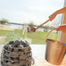 Hand holding Geneva ladle over HUUM heater inside St. Moritz sauna, framed by stunning lakeside background.
