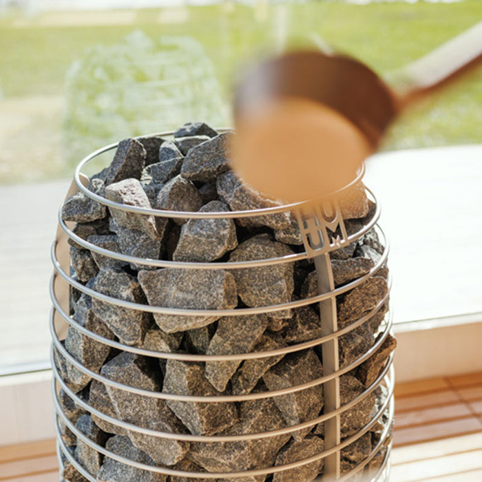 Close-up of HUUM stone sauna heater inside Geneva St. Moritz cabin, with natural light streaming in through large corner glazing.