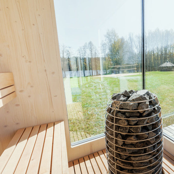 Geneva St. Moritz sauna interior with HUUM heater and panoramic glass walls offering an immersive nature view.