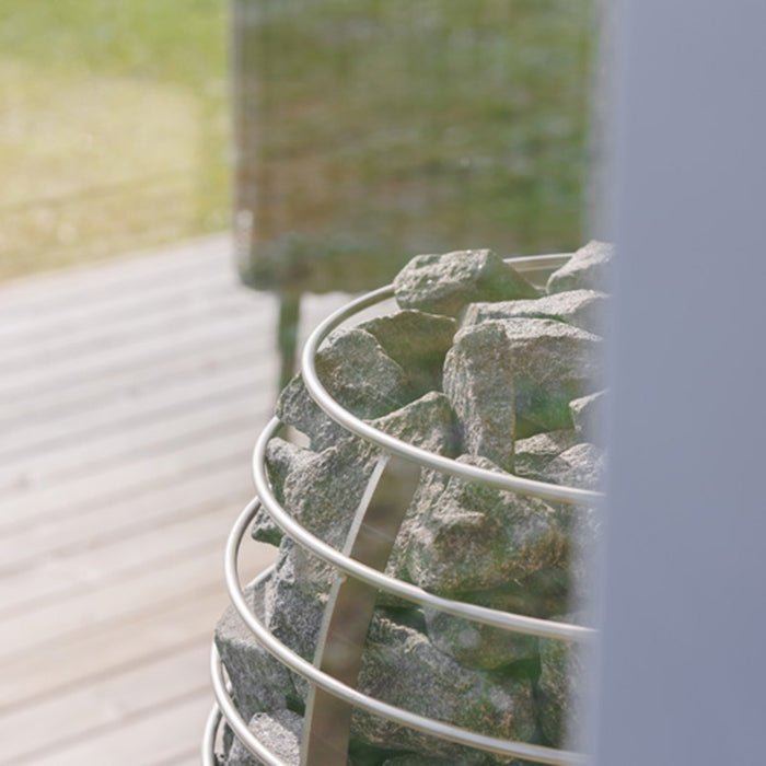 Artistic close-up of HUUM sauna heater through window glass in Geneva St. Moritz cabin, capturing natural detail.