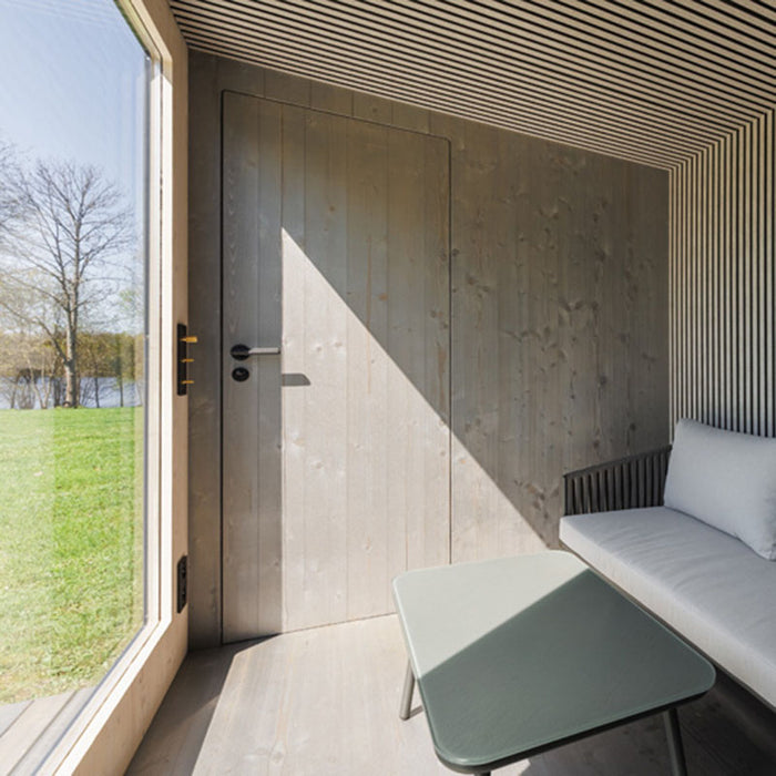 Minimalist interior with full-height wooden door and lounge seating inside Geneva St. Moritz outdoor sauna and shower cabin.