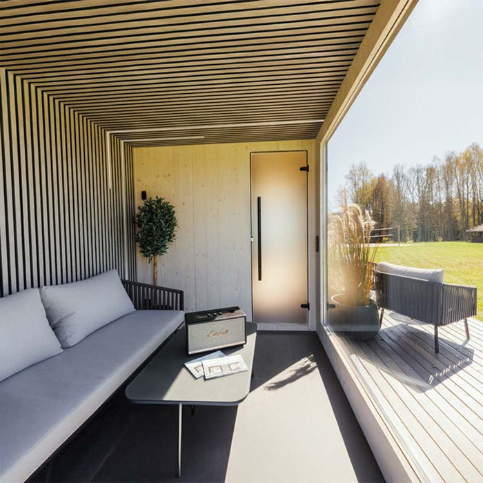 Cosy covered terrace of Geneva St. Moritz outdoor sauna, featuring soft seating, glass wall views, and minimal Nordic-inspired design details.