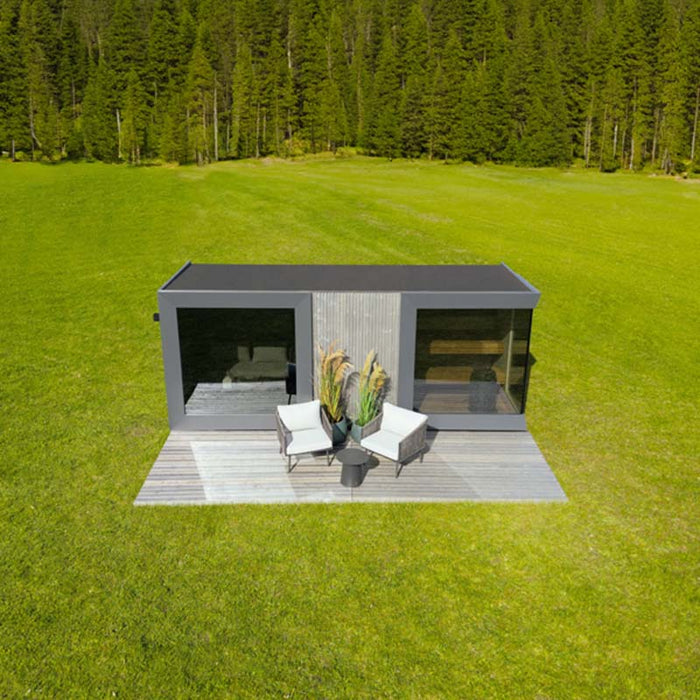 Front view of the St. Moritz outdoor sauna by Geneva, showcasing symmetrical glass design, wooden terrace and outdoor seating in a lush green meadow.