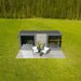 Front view of the St. Moritz outdoor sauna by Geneva, showcasing symmetrical glass design, wooden terrace and outdoor seating in a lush green meadow.