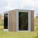 Side angle of the Zermatt outdoor sauna showing dual full-height tinted glass panels and vertical timber exterior in a natural garden setting.