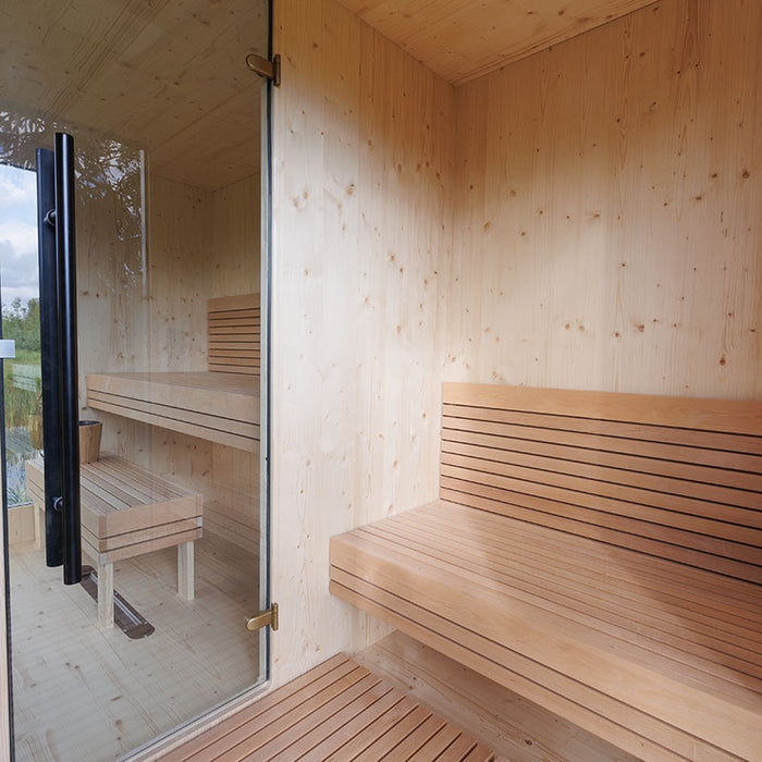 Spacious interior of the Zermatt outdoor sauna with minimalist wooden benches, glass door entrance, and views of the surrounding countryside.