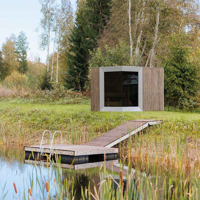 Contemporary Zermatt sauna cabin with changing room nestled beside a peaceful pond, connected by a wooden deck walkway in a lush landscape.