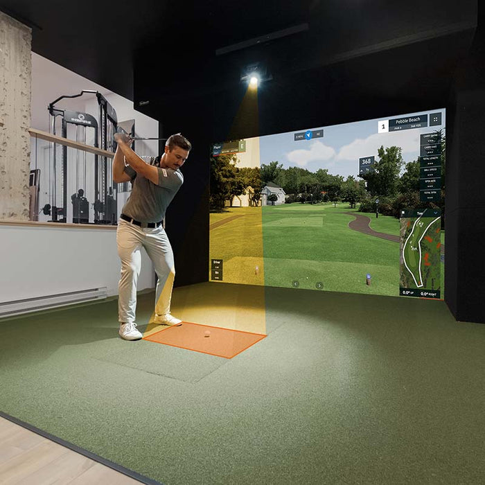 Golfer mid-swing using GolfIn IDRA II Launch Monitor in indoor golf simulator, showing course projection and real-time shot tracking with advanced swing metrics.