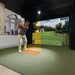 Golfer mid-swing using GolfIn IDRA II Launch Monitor in indoor golf simulator, showing course projection and real-time shot tracking with advanced swing metrics.