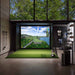 Luxurious golf simulator setup with a large screen displaying a scenic golf course, featuring various golfing equipment and a lush outdoor view.