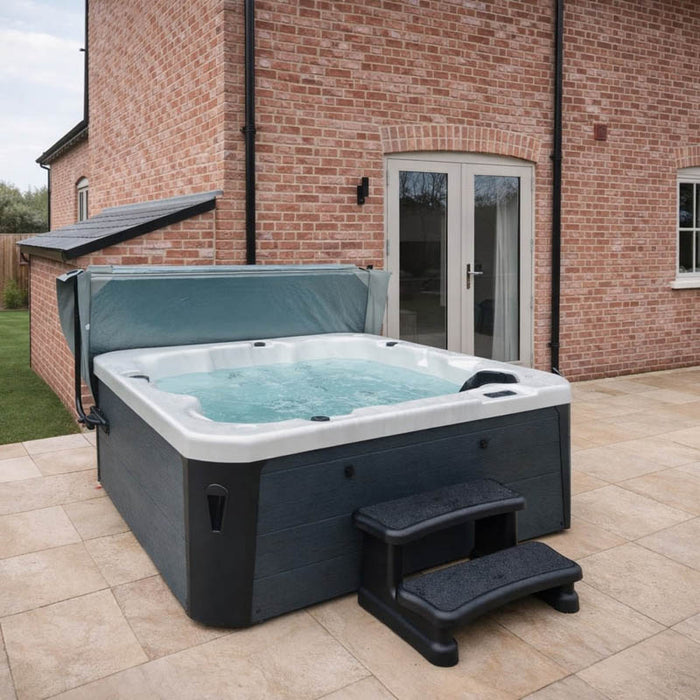 H2O Azure 5-Person Hot Tub installed against a brick house exterior with cover lifter raised and entry steps, dark grey woodgrain cabinet