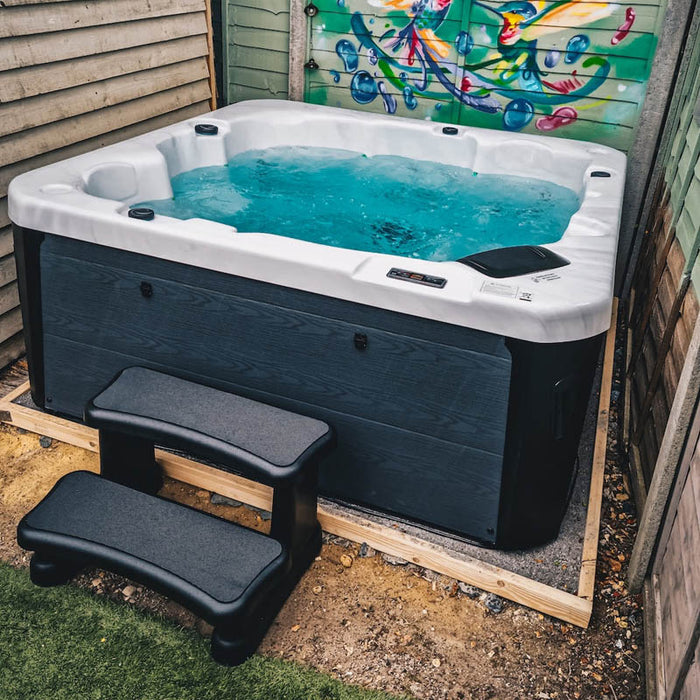 H2O Azure 5-Person Hot Tub in a compact enclosed outdoor space with teal blue water, dark navy cabinet and colourful mural backdrop