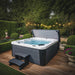 H2O Azure 5-Person Hot Tub on wooden decking in a formal garden with topiary hedging and fairy lights, cover lifter raised and entry steps visible