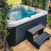 H2O Azure 5-Person Hot Tub on a garden patio with raised wooden border surround, teal blue water, dark grey cabinet and entry steps