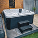 H2O Azure 5-Person Hot Tub installed in a gravel and slate bordered garden area against a brick wall, dark navy cabinet with white acrylic shell and entry steps