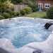 Close-up of the H2O Azure 5-Person Hot Tub water surface with jets running, showing white acrylic shell and built-in waterfall feature with garden background