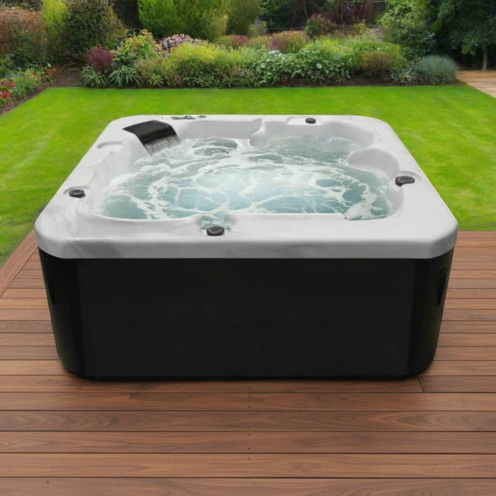 H2O Azure 5-Person Hot Tub on a wooden deck with black cabinet, jets and fountain running, white acrylic shell against a landscaped UK garden