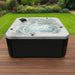 H2O Azure 5-Person Hot Tub on a wooden deck with black cabinet, jets and fountain running, white acrylic shell against a landscaped UK garden
