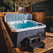 H2O Azure 5-Person Hot Tub on wooden decking at night with cover lifter raised, dark grey woodgrain cabinet, teal water and entry steps