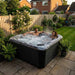 Couple relaxing in the H2O Coral 5-Person Hot Tub in a UK garden in the evening, jets on and steam visible
