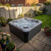 H2O Coral 5-Person Hot Tub in a UK garden at dusk surrounded by hydrangeas and potted plants, steam rising from the water