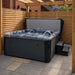 H2O Coral 5-Person Hot Tub open with cover lifter raised under a wooden pergola, jets and fountain active, dark cabinet finish