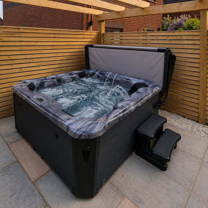 H2O Coral 5-Person Hot Tub under a wooden pergola with fountain jets running, cover lifter in use, dark cabinet and steps