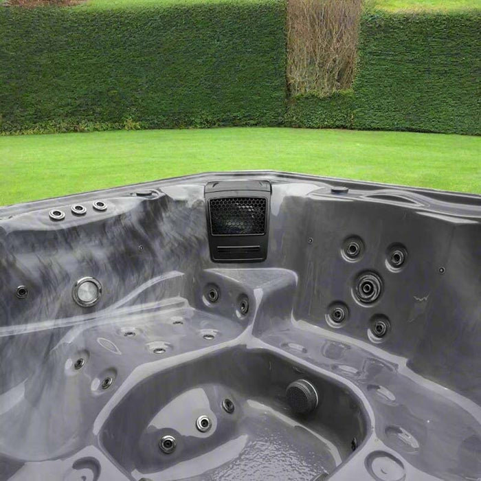 H2O Vortex 6-Person Hot Tub grey interior showing integrated AquaSonic Bluetooth speaker unit and jet layout with garden hedge backdrop
