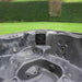 H2O Vortex 6-Person Hot Tub grey interior showing integrated AquaSonic Bluetooth speaker unit and jet layout with garden hedge backdrop