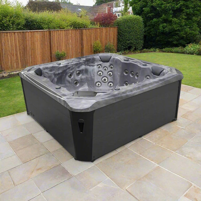 H2O Vortex 6-Person Hot Tub with grey marbled shell and charcoal cabinet installed on a stone patio in a fenced UK garden
