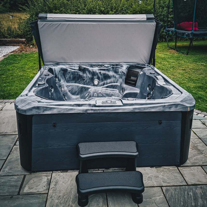 H2O Vortex 6-Person Hot Tub with grey marbled shell and charcoal cabinet, cover fully open revealing dry interior and seating layout on a garden patio
