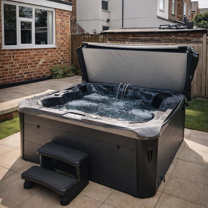 H2O Vortex 6-Person Hot Tub with grey shell and dark charcoal cabinet, cover open showing active jets, installed on a paved patio in a UK suburban garden with entry steps