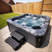 H2O Vortex 6-Person Hot Tub with grey marbled shell and dark cabinet, jets fully active with churning water, installed on a patio with entry steps in a UK suburban garden