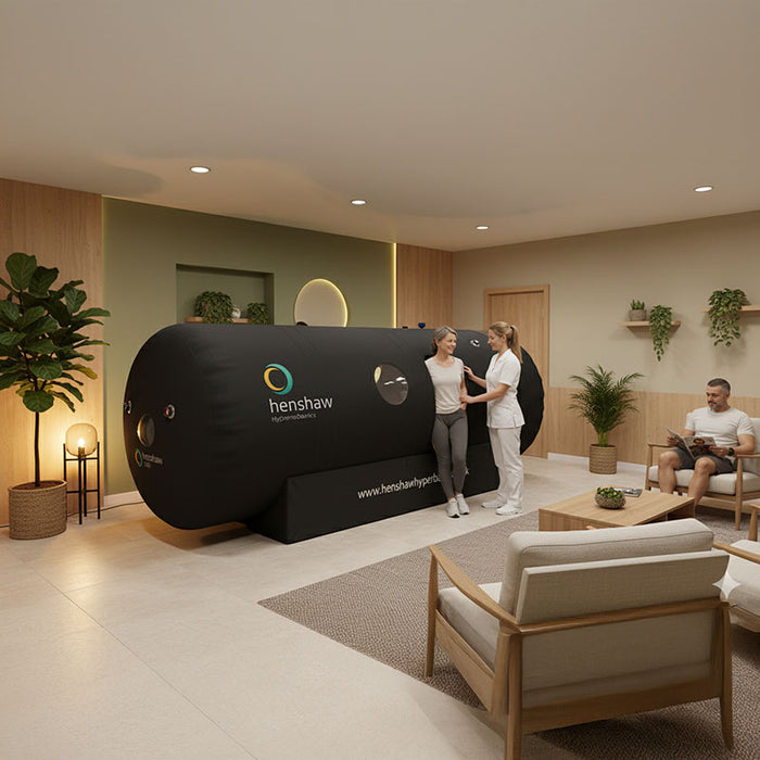 Therapist assisting a woman after a session inside the Henshaw 1662 Hyperbaric Oxygen Chamber, with another patient relaxing in a calming clinic.