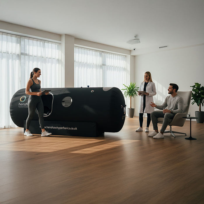 Active wellness consultation with the Henshaw 1662 Hyperbaric Oxygen Chamber, fitness client, and professionals in a bright modern clinic.