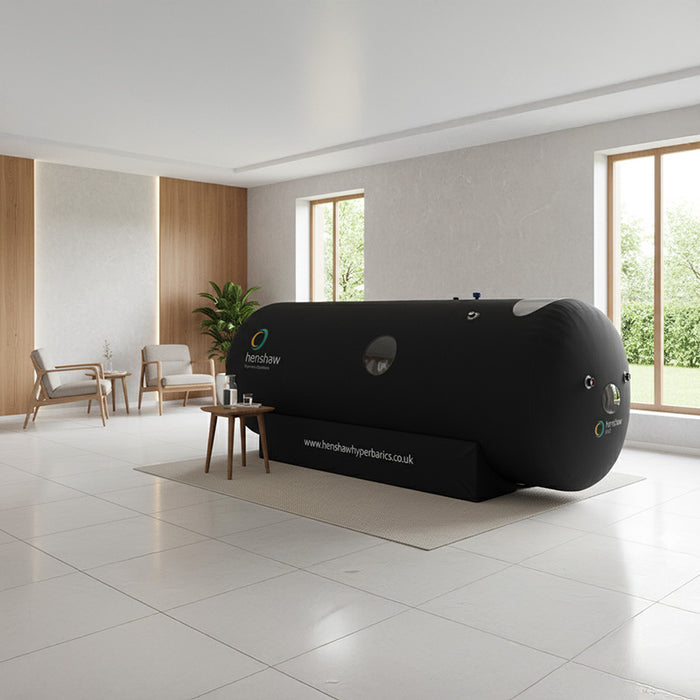 Henshaw 1662 Hyperbaric Oxygen Chamber in a modern wellness lounge with wooden panel features and two armchairs for relaxing sessions.