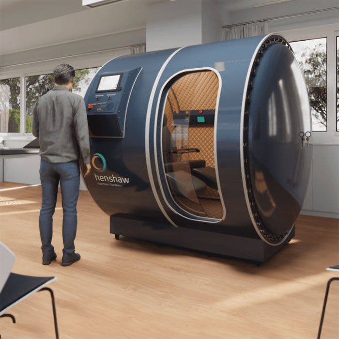 Henshaw Duoplace Chamber set up in a clean clinical space with a man inspecting its transparent door and digital control panel for therapeutic use.