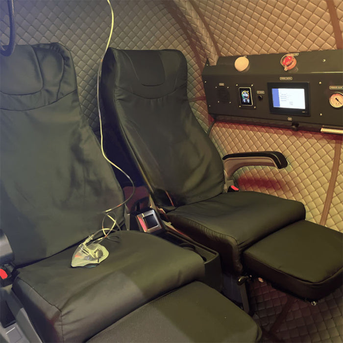 Interior view of the Henshaw Duoplace Hyperbaric Oxygen Chamber featuring two luxury reclining seats, control panel, and quilted walls for dual-person oxygen therapy.
